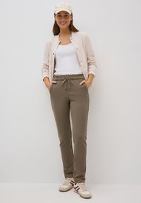 Lichtroze bomberjack, witte tanktop en olijfgroene broek met elastische tailleband. Witte en beige sneakers met kastanjebruine accenten. Casual outfit.
