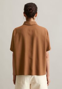 Korte mouwen, geknoopte shirt in bruine stof met een gladde textuur en een losse pasvorm, gecombineerd met hooggewende crèmekleurige broeken.