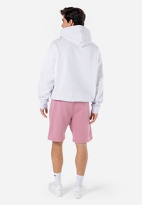 Hvid hætte Sweatshirt med en afslappet pasform, parret med pink shorts. Outfittet har et enkelt design og er lavet af blødt stof.