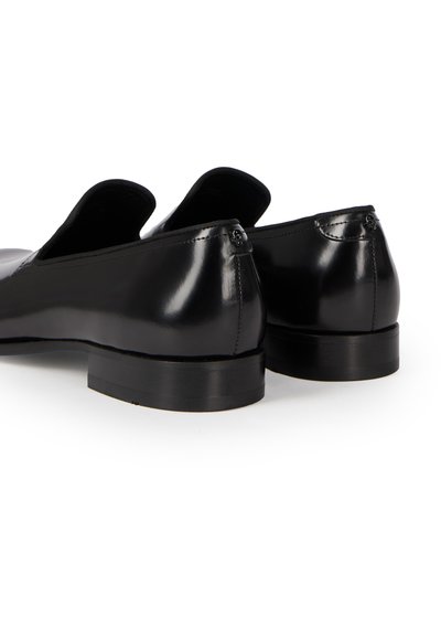 Chaussures de ville en cuir noir brillant, à enfiler, avec talons bas, vues de dos sur fond blanc.