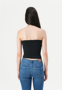 Top negro sin tirantes con un diseño ajustado, combinado con jeans skinny de color azul claro que presentan un estilo clásico de cinco bolsillos.