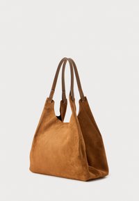 Hnědá semišová taška přes rameno se dvěma koženými uchy a otevřeným horním okrajem. Má měkkou texturu a šikmé strany pro volný, povislý tvar.