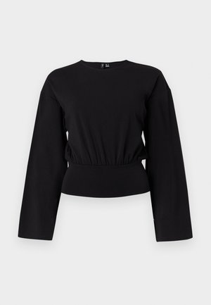 Μαύρο τοπ με μακριά μανίκια, στρογγυλή λαιμόκοψη, ζωνάκι στη μέση και ελαφρώς χαλαρή εφαρμογή σε απλό ανοιχτό φόντο.