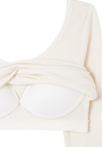 Kremowy, prążkowany top z długim rękawem, częściowo podniesiony, aby odsłonić wbudowany biały biustonosz z podszewką i wsparciem w formie fiszbin.