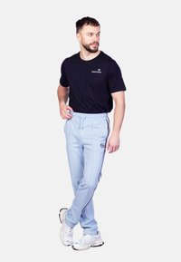 Lichtblauwe joggingsbroek met zwarte zijstrepen en geborduurd logo, gecombineerd met een aansluitend zwart T-shirt, gedragen met witte sportschoenen.