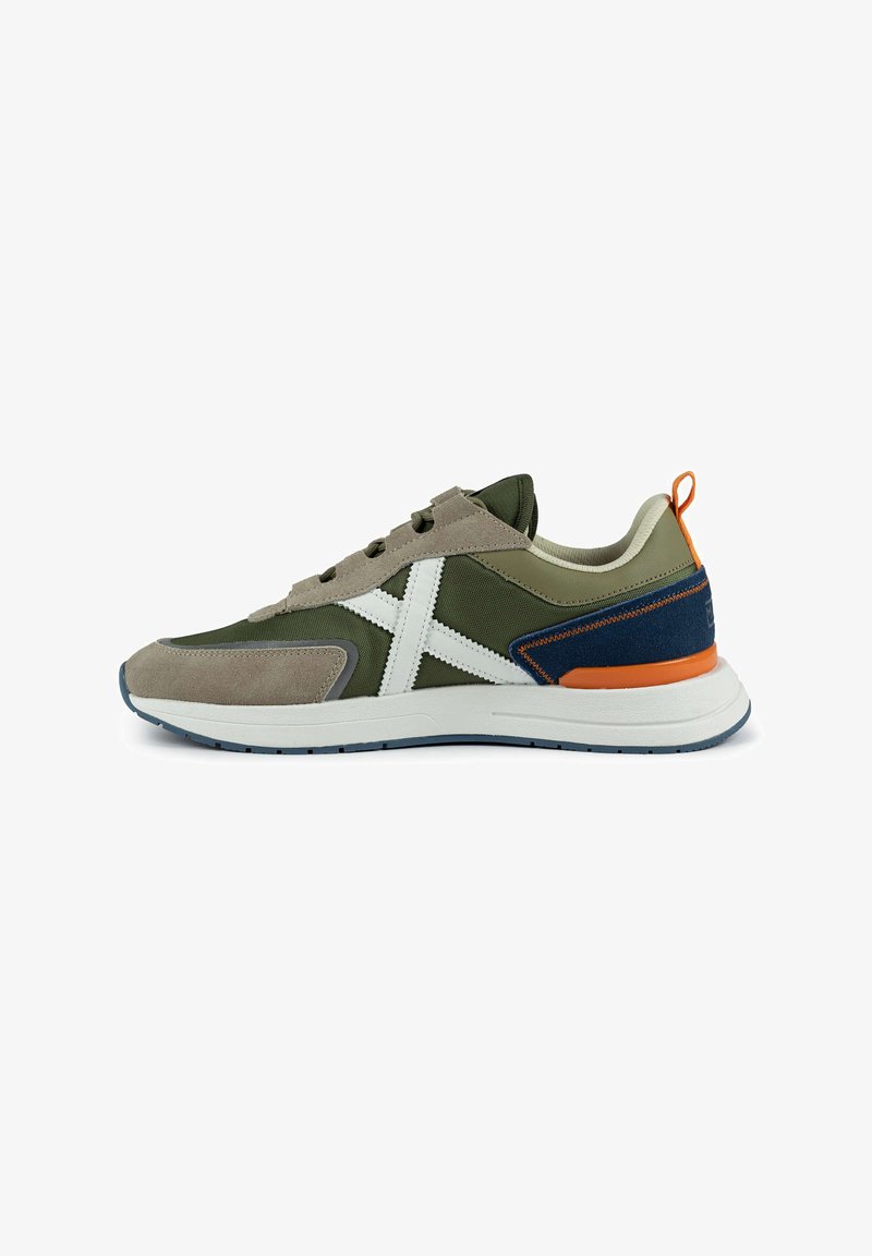 Green and tan sneaker with a white logo, suede and mesh materials, padded collar, orange accent, and a textured rubber sole.