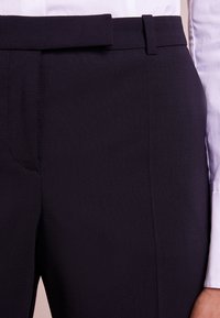 Marineblauwe op maat gemaakte broek met een gladde stofstructuur, slim fit en een platte voorkant. Voorzien van een riemlus en subtiele zijzakken.