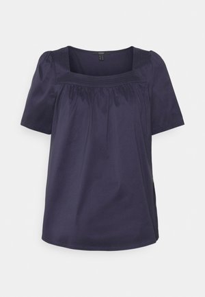 Blouse bleu marine à manches courtes avec un col carré et un tissu froncé sous le empiècement.