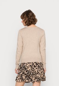 Beige neulepaita, jossa pitkät hihat, resorit hihoissa ja helmassa, pyöreä pääntie. Alla näkyy kerroksittain liehuva hame, jossa musta leopardikuvio.