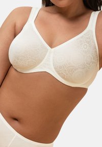 Crème kleurige kanten beha met bloemmotieven, beugelondersteuning, verstelbare bandjes en een gladde textuur. Ontworpen voor comfort en pasvorm.