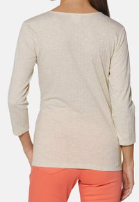 Jasno beżowa bluzka z długim rękawem o fakturowanym splocie, okrągłym dekolcie i rękawach o długości za łokieć, zestawiona z koralowymi spodniami.