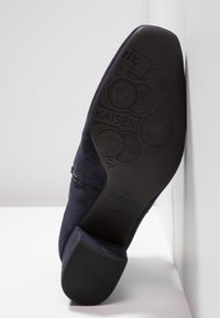 Semelle d'une chaussure habillée en daim bleu marine avec des motifs de pièces embossés, texte « KAISER » et taille 41½ par Peter Kaiser.