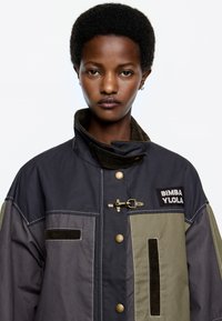 Kleurgeblocte jacket met donker marineblauw, olijfgroen en lichtgrijze panelen. Voorzien van een corduroy kraag, messing hardware en een logo patch.