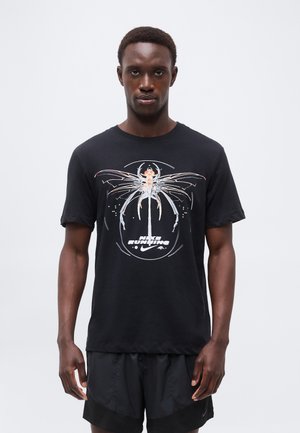 Man draagt een zwart Nike Running T-shirt met een abstract insectenmotief en zwarte sportshorts, staand tegen een effen lichte achtergrond.