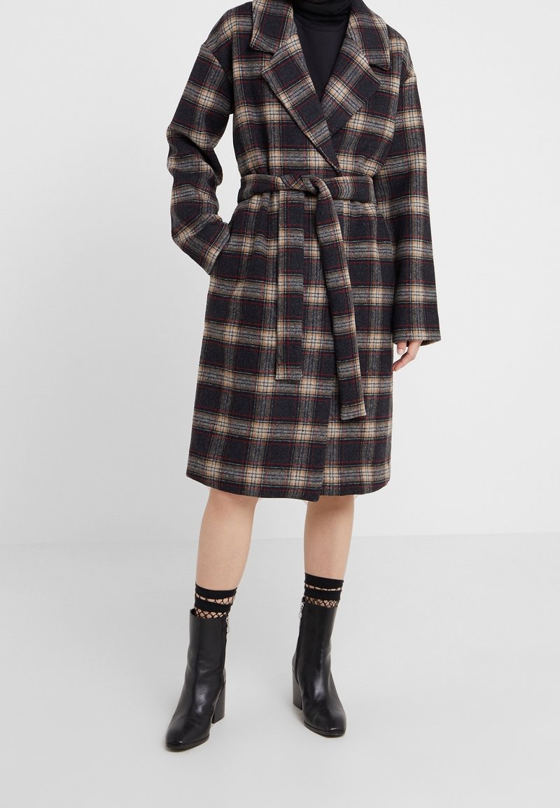 Abrigo largo de mezcla de lana con estampado a cuadros y cintura con cinturón, que presenta un gran cuello, mangas anchas y una combinación de colores negro, marrón y beige.