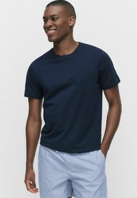 Marineblauwe T-shirt met korte mouwen en een borstzak, gemaakt van zachte stof, gecombineerd met lichtgestreepte shorts. Gladde textuur, normale pasvorm.