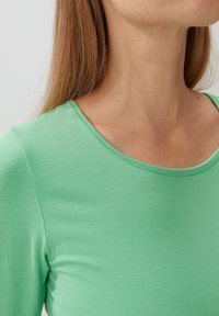 Groene, aangesloten lange mouw top gemaakt van een gladde, rekbare stof. Bevat een ronde halslijn met zichtbare stikseldetails.