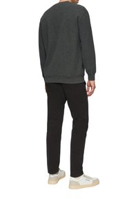 Pull en maille gris avec un col rond, associé à un pantalon noir et des baskets blanches. La coupe est décontractée, mettant l'accent sur le confort et la simplicité.