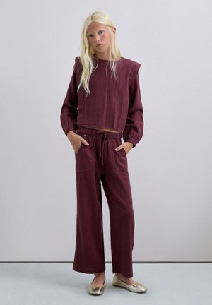 Suéter corto burdeos con textura acanalada y hombros anchos, combinado con pantalones de pierna ancha a juego que cuentan con bolsillos y una cintura con cordón.