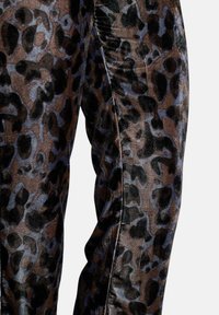 Samtleggings mit einem braun-schwarzen Leopardenmuster und dezenten blauen Akzenten; glatte Textur und figurbetontes Design.