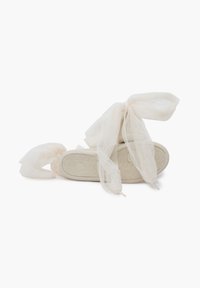 Light beige sandals with tulle ribbons tied in bows at the ankle, showcasing a simple sole design and a fashionable, airy appearance.