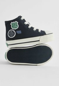 Granatowe kanwasowe sneakersy na wysokiej podeszwie z białą gumową podeszwą. Oferują wyszywane naszywki: "Mistrzowie Wschodniej Ligi", "Mistrzowie 08" oraz "92". Teksturowana podeszwa.
