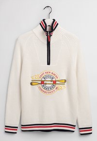 Sweter dzianinowy w kolorze kremowym z zamkiem przy szyi, z logo sportowym w kolorze czerwonym, żółtym i niebieskim. Prążkowany kołnierz i mankiety w paski.