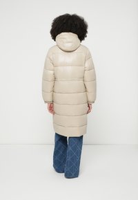 Casaco acolchoado bege com capuz, com um design acolchoado e mangas compridas, combinado com calças de ganga flare com padrão de diamante.