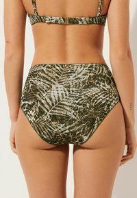 Högmidjad bikiniunderdel med grön, brun och svart djur- och lövmönster, med mjuk textur och kontrasterande kant.