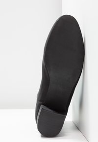 Calzado negro con una parte superior suave y suela texturizada. Presenta un ligero tacón y puntera redonda. La suela muestra surcos para mayor agarre.