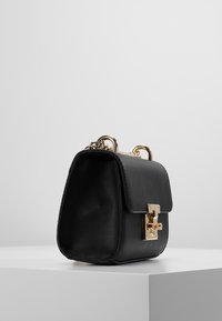 Borsa in pelle nera con una forma strutturata, hardware dorato e un clasp frontale. Presenta una tracolla a catena e una superficie liscia.