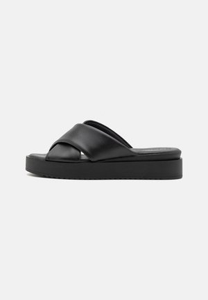 Schwarze Rutsch-Sandalen aus glattem Leder, mit einem Kreuzriemen-Design und einer dicken, flachen Sohle mit strukturierten Rändern.