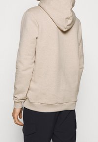 Sudadera beige con una textura suave, capucha y puños y dobladillo acanalados. Combinada con pantalones cargo oscuros, mostrando un ajuste relajado y informal.