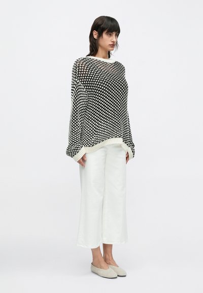 Μπλούζα πλεκτή σε ασπρόμαυρο με άνετη εφαρμογή, στρογγυλή λαιμόκοψη και μακριά μανίκια. Συνδυάζεται με λευκό παντελόνι φαρδιάς γραμμής και γκρι μπαλαρίνες.