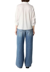 Weißes Langarmhemd mit einem Rückenteil, kombiniert mit weit geschnittenen, hellblauen Jeans mit verwaschenem Finish, Gesäßtaschen und lockerer Passform.