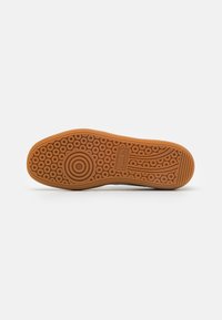Suola di scarpa in gomma con un motivo circolare, caratterizzata da una trama liscia arancione-marrone e un grande logo al centro. Bordo curvo visibile.