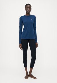Navy long-sleeve shirt with a round neck and a subtle logo. Paired with fitted black leggings, both made from soft, stretchy fabric.