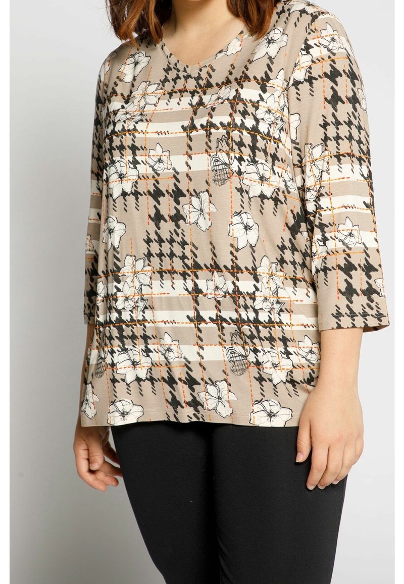 Beige mönstrad topp med blommor och houndstooth-design och orange detaljer. Tillverkad av mjukt tyg, har den trekvartslånga ärmar och V-ringning.