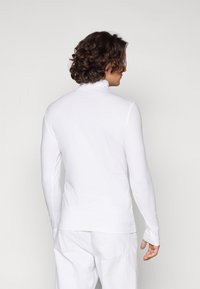 Suéter de manga larga blanco con cuello alto, hecho de una tela suave y elástica. Presenta una silueta ajustada y un diseño sin costuras en el cuello y los puños.