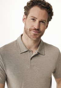 Grå polo skjorta med ribbad krage, korta ärmar och två knapprad. Materialet verkar mjukt och texturerat. Enkel, enfärgad design.