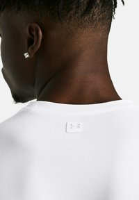 Camiseta blanca de manga corta con un acabado texturizado, un collar plano y una pequeña etiqueta blanca en la parte trasera, cerca del cuello.