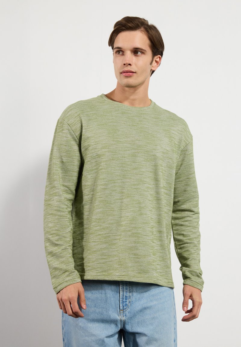 T-shirt à manches longues en vert clair, en tissu texturé. Présente une coupe décontractée et un design minimaliste. Associé à un jean en denim bleu clair.
