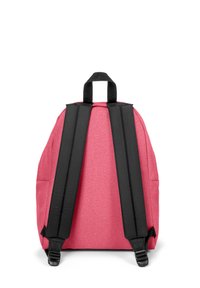Pink backpack with a matte finish, black padded straps, and a top handle. Features a rounded shape and side compartments for storage.