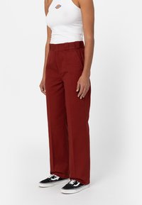 Vida med vida ben i rostig röd bomull, med en slät yta och framveck. Kombinerad med en vit linne och svarta snörskor.