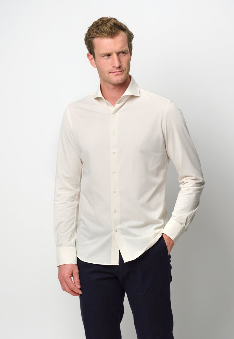 Camicia button-up beige chiaro in una vestibilità slim, con colletto aperto e maniche lunghe. Il tessuto appare liscio con una leggera lucentezza.