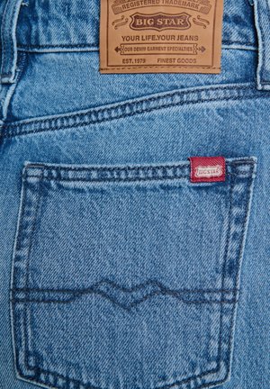 Jasnoniebieskie dżinsy z denimu z skórzaną metką z napisem "BIG STAR" oraz małą czerwoną łatką, podkreślone kontrastowym przeszyciem na tylnej kieszeni.