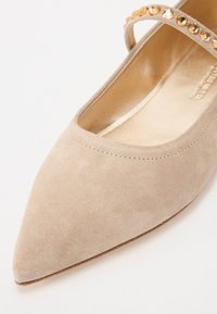 Ballerines en suède beige à bout pointu avec une sangle décorative ornée d'accents ronds réfléchissants sur le dessus.