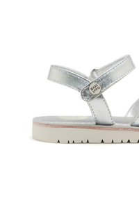 Sandalias metálicas plateadas con tiras entrecruzadas, plantilla acolchada y suela de goma blanca con un patrón texturizado.