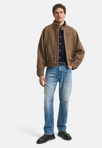 Brun herringbone zip-jacka med hög krage, matchad med ljusblå jeans och svarta skor. Strukturerad tyg och avslappnad passform.