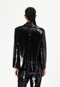 Svart glitrende blazer med en strukturert design, som har notched krage og lange ermer, reflekterer lys med en blank tekstur.